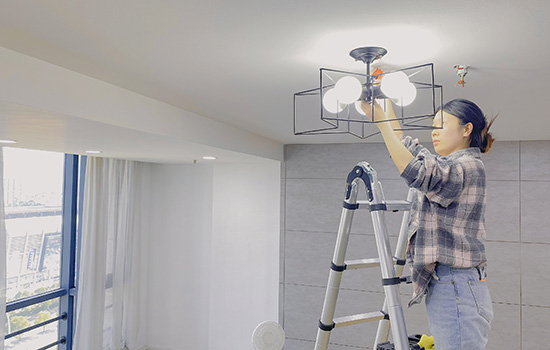 A girl stands on a double telescopic ladder and repairs a light bulb